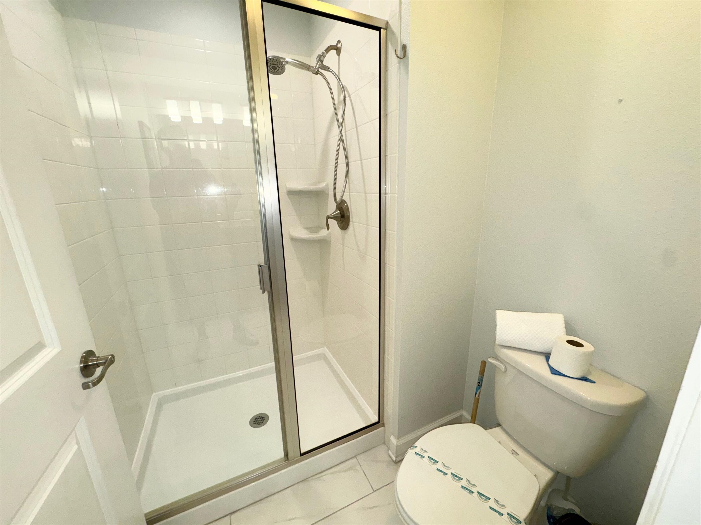 A bathroom with a glass-enclosed shower, a toilet, and a white tiled floor.