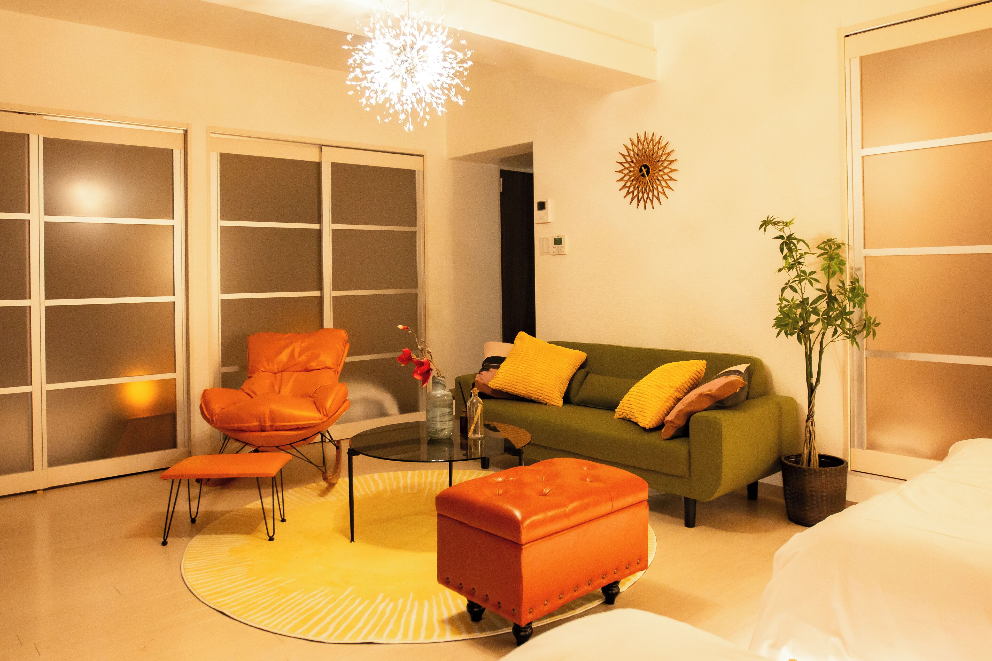 A modern living room with a sofa, armchair, ottoman, and a potted plant.