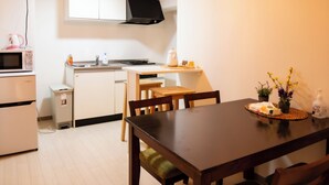 Une cuisine compacte équipée d’un four à micro-ondes, d’une cuisinière, d’un évier et d’une petite poubelle. On y trouve une table à manger en bois, avec des chaises, et une petite plante en pot posée sur la table.