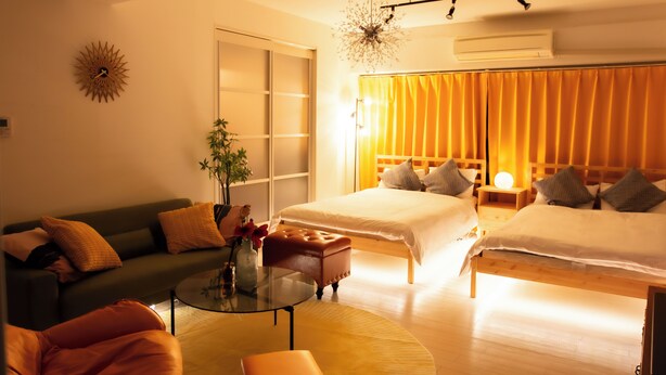 Une chambre d’hôtel avec deux lits, un canapé, une table basse et une petite table ornée d’un vase et de fleurs.