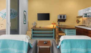 Quarto de hotel compacto com cozinha compacta, televisão na parede e cama com colcha azul-turquesa e branca.