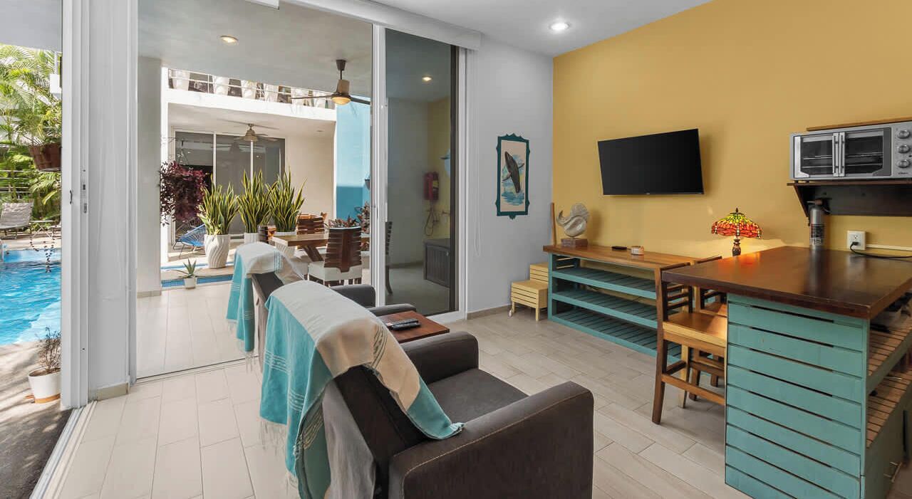 A modern living room with a pool view, a dining area, and a kitchen with a microwave.