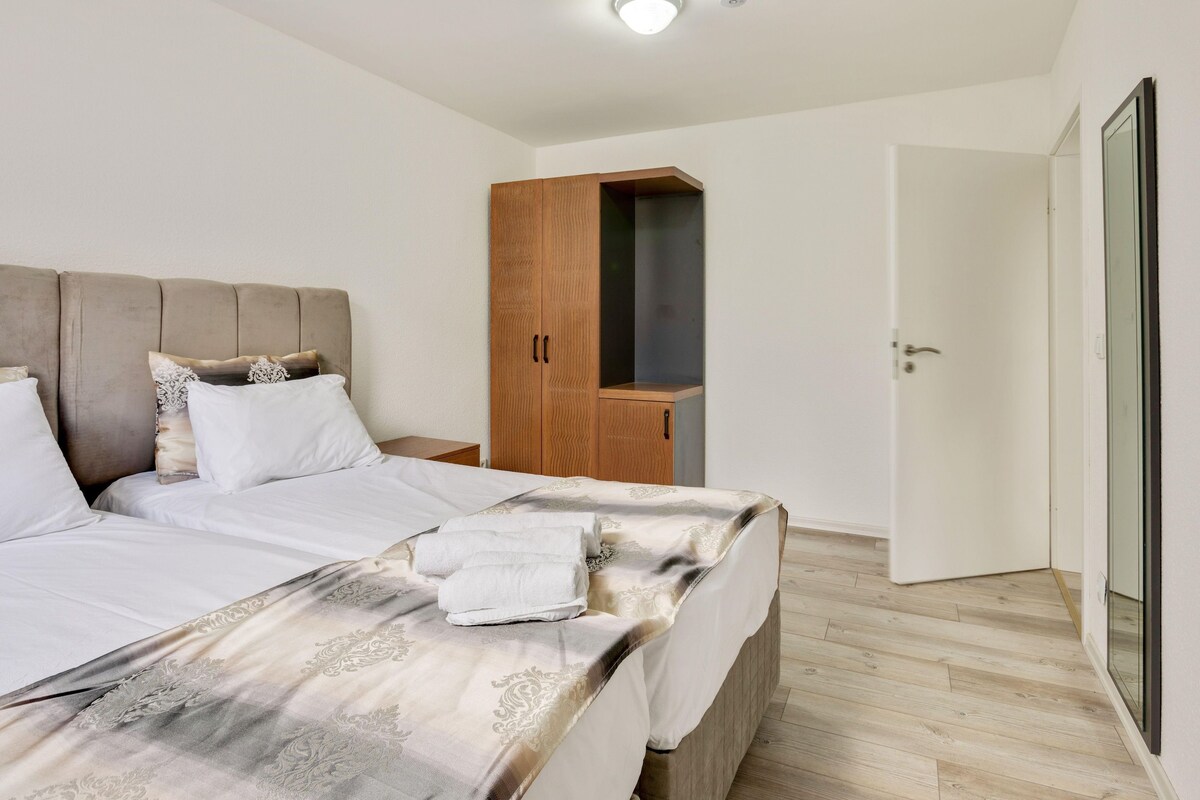 A bedroom with a large bed, wooden wardrobe, and a door leading to another room.