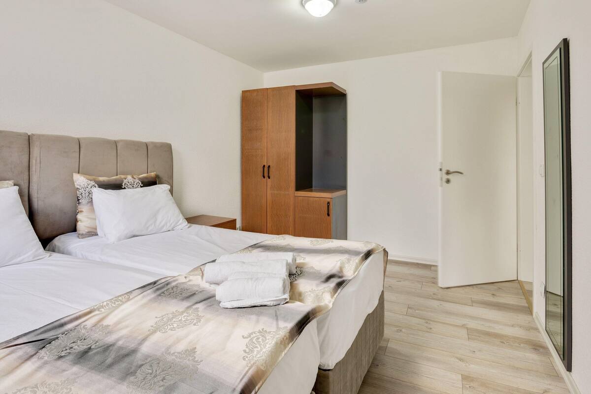 Quarto com cama grande, guarda-roupa de madeira e porta que dá para outro cômodo.