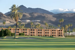 Camp de golf amb un hotel al fons, envoltat de muntanyes i palmeres.