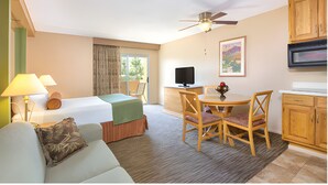 Habitación de hotel con cama, escritorio, silla, televisor y ventilador de techo.