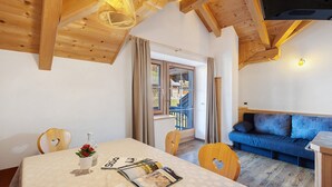 A cozy room with a wooden ceiling, a sofa, a dining table with a magazine, and a window with curtains. - Apartment 'Rît' with Mountain View, Shared Terrace and Wi-Fi (La Valle)