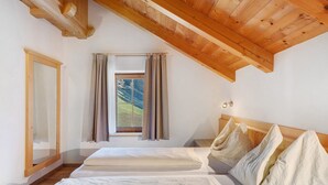 A bedroom with a sloped ceiling, a window with curtains, and a bed with pillows. - Apartment 'Rît' with Mountain View, Shared Terrace and Wi-Fi (La Valle)