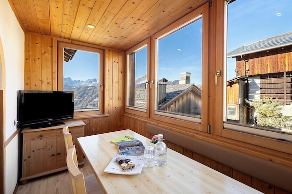 A wooden cabin with a television, table, and windows overlooking a mountainous landscape.