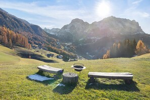 Een bergachtig landschap met een heldere lucht, een houten bankje en een metalen barbecue in de voorgrond.