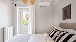 A bedroom with a bed, a radiator, an air conditioning unit, a hanging light fixture, and a view through an open door. - Family Escape in Chalandri -Parnassidos 10 (Chalandri)
