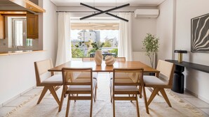 A modern dining area with a wooden table and chairs, a view through a window, and a plant on the side. - Family Escape in Chalandri -Parnassidos 10 (Chalandri)