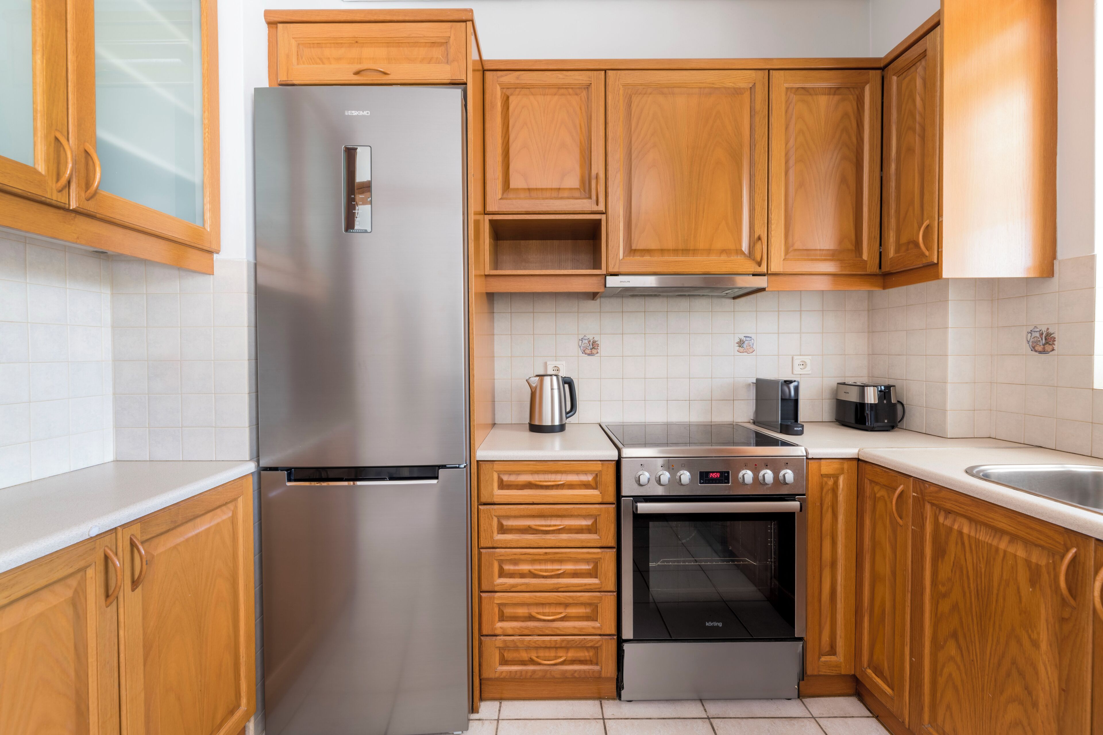Eine Küche mit Holzausstattung, einem Edelstahlkühlschrank, einer Kaffeemaschine, einem Toaster und einem Backofen.