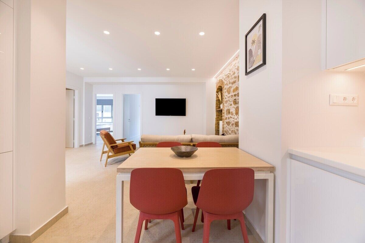 Uma sala de estar moderna com um sofá, uma mesa de jantar com cadeiras, uma TV na parede e uma parede de destaque em pedra.