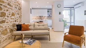 A modern living room with a stone wall, a beige sofa, a wooden coffee table, and a brown armchair. - Psyrri Hideout · Chic 2BR Apartment (Athina)