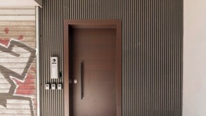 A modern entrance with a brown door, a keypad, and a vertical paneling design. - Psyrri Hideout · Chic 2BR Apartment (Athina)