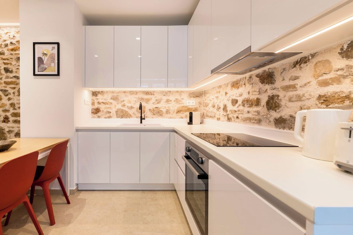 Cuina moderna amb armaris blancs, un frontal de pedra i forn encastrat.