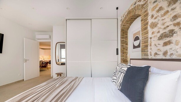 A bedroom with a large bed, a stone wall, a wardrobe, and a mirror. - Psyrri Hideout · Chic 2BR Apartment (Athina)