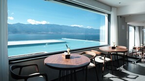 A modern hotel room with a large window offering a view of a pool and mountains. There are two round wooden tables with chairs. - Dali Puyu VILLA Cliff Seaview Hotel (Dali)