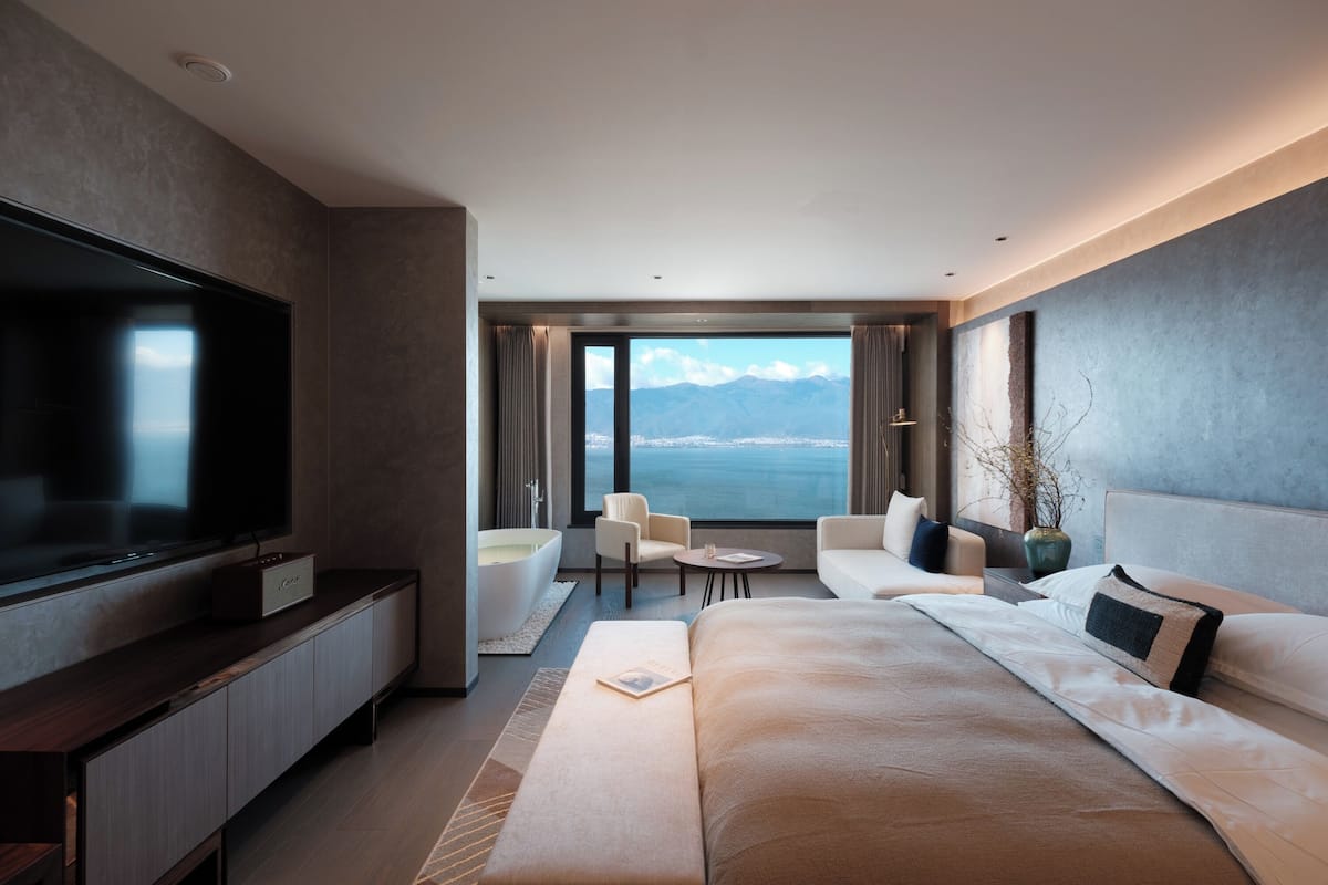 Une chambre d’hôtel moderne dotée d’un grand lit, d’une télévision à écran plat, d’un coin salon avec vue sur la mer et d’une grande fenêtre.