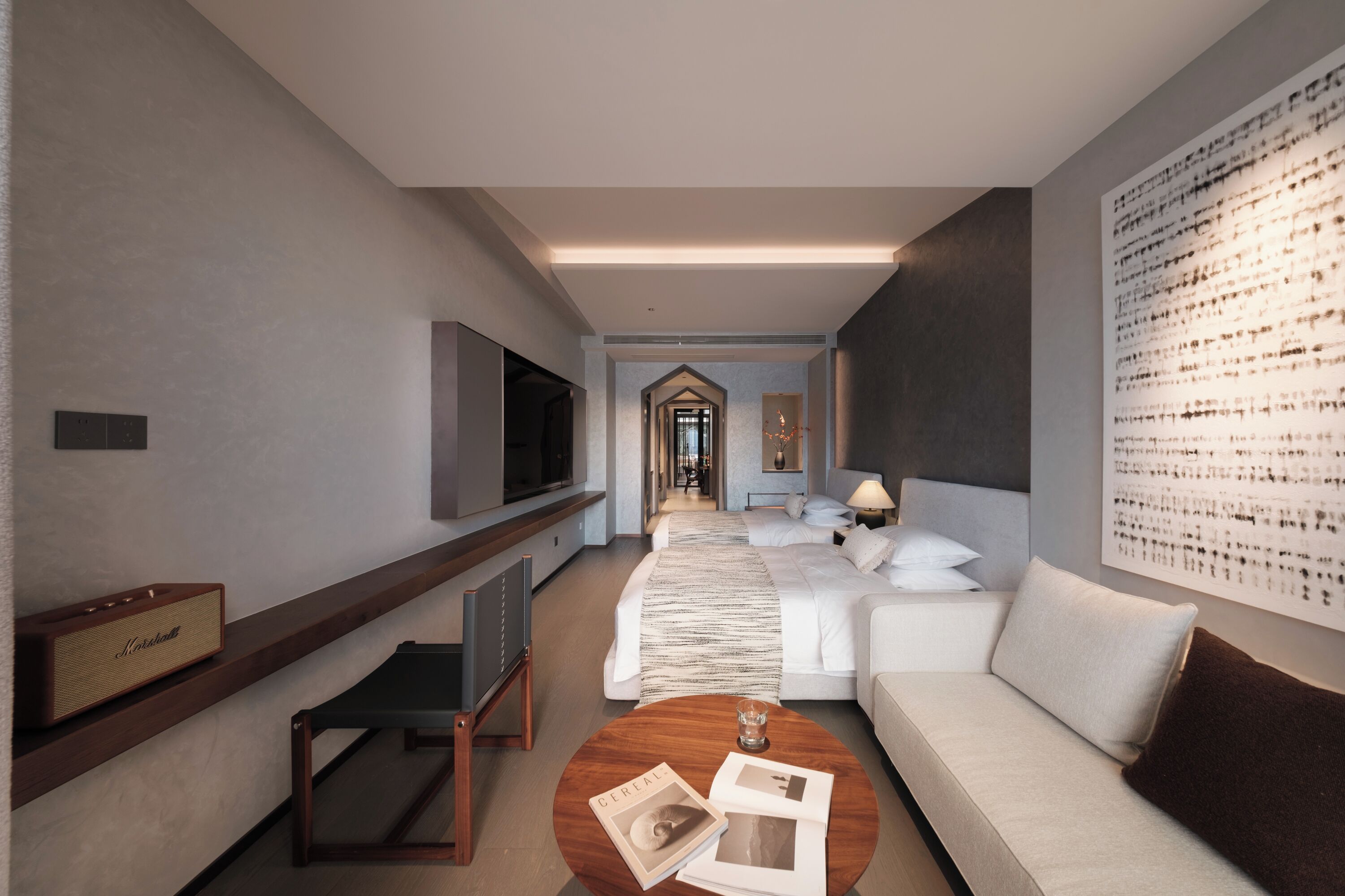 A modern hotel room with a large bed, a sofa, a TV, a coffee table, and a wall art piece.