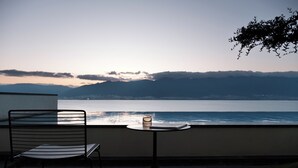 A balcony with a chair and a small table, overlooking a body of water and distant mountains. - Dali Puyu VILLA Cliff Seaview Hotel (Dali)