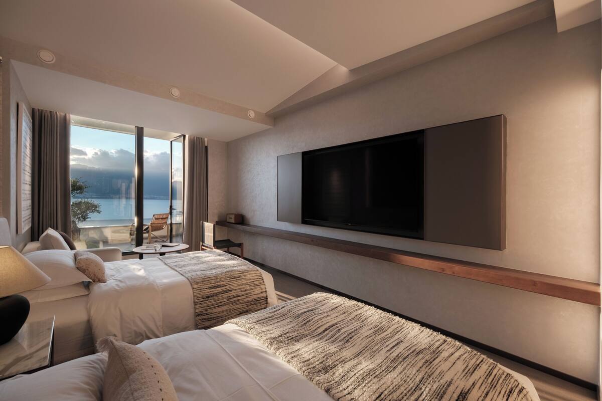 Une chambre d’hôtel moderne avec deux lits, une grande télévision et un balcon offrant une vue sur la mer.