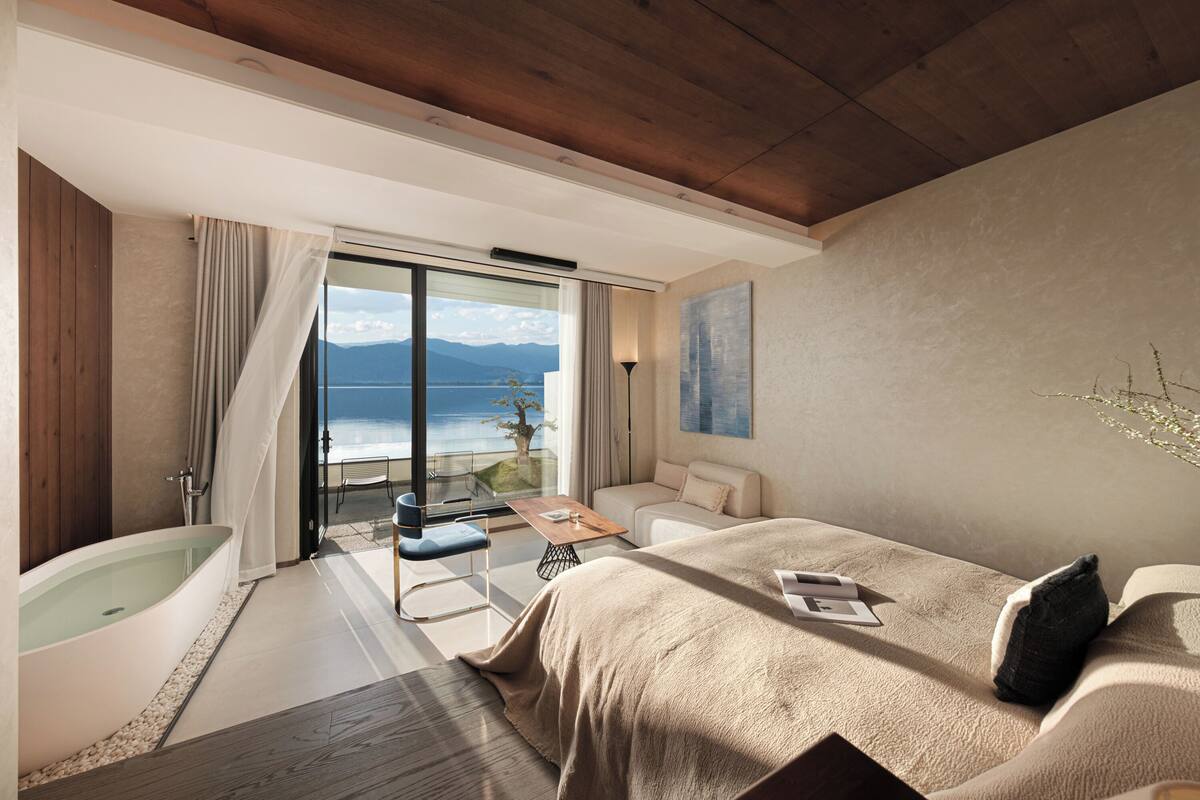 Une chambre d’hôtel moderne dotée d’un grand lit, d’une baignoire, d’un balcon avec vue sur la mer et d’un coin repas.