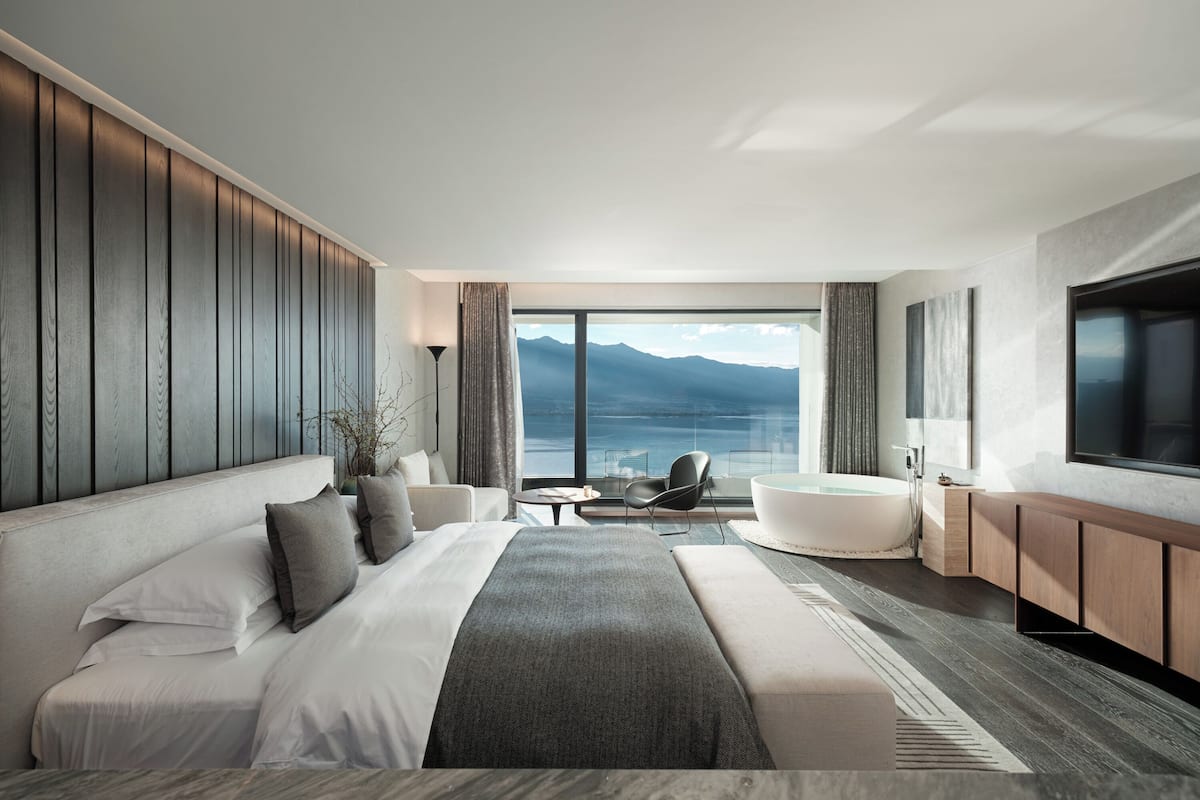 Une chambre d’hôtel moderne dotée d’un grand lit, d’un coin salon avec vue sur la mer et d’un téléviseur fixé au mur.