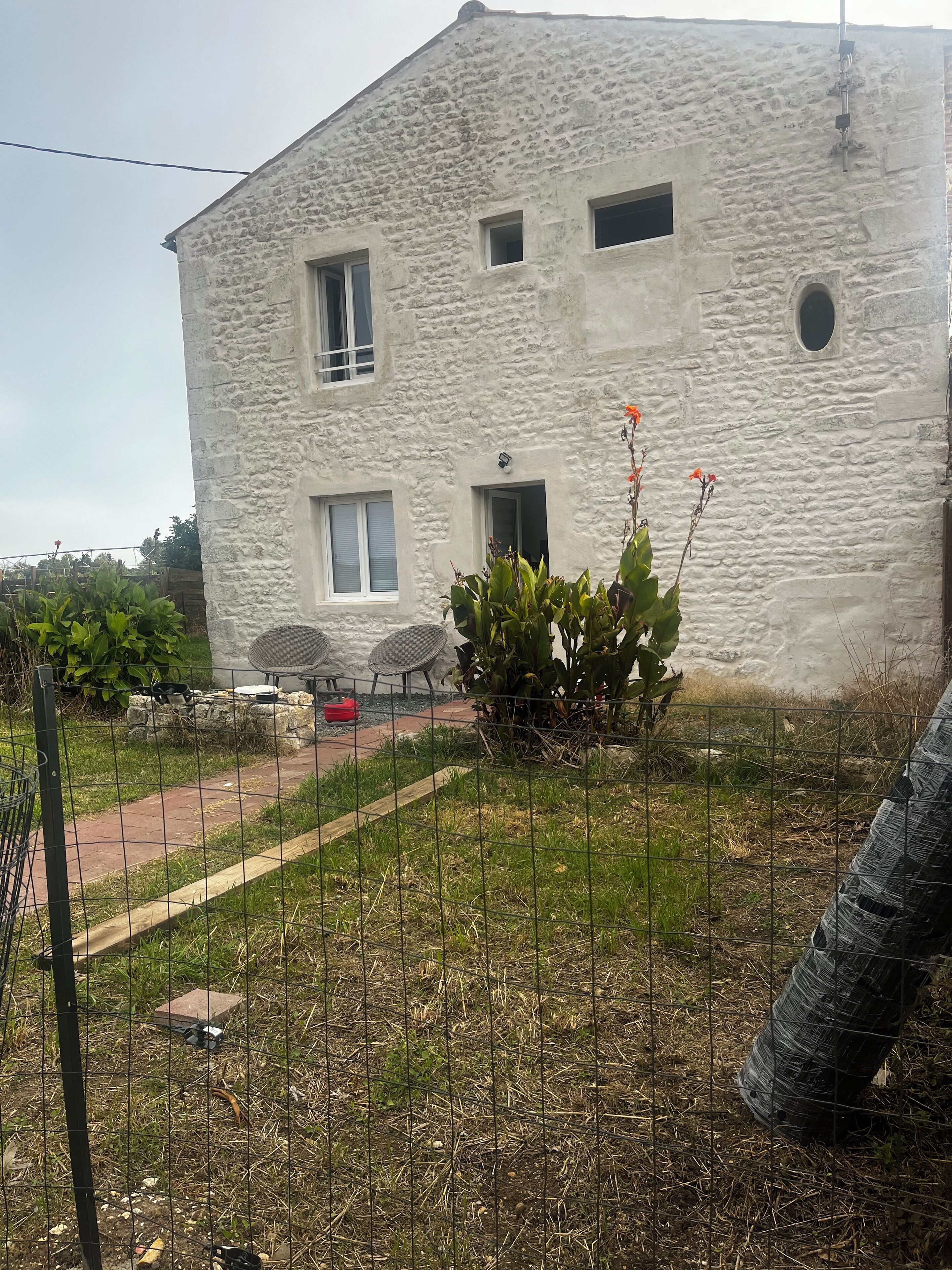 Un edificio de piedra con un patio empedrado, mesas al aire libre y un jardín vallado.
