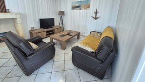 A living room with two black leather sofas, a wooden coffee table, a TV on a wooden stand, a lamp, and a wall-mounted anchor decoration. - Between land and sea (Marennes-Hiers-Brouage)