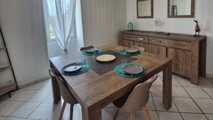 A dining area with a wooden table set for four, a chandelier, and a kitchen in the background. - Between land and sea (Marennes-Hiers-Brouage)
