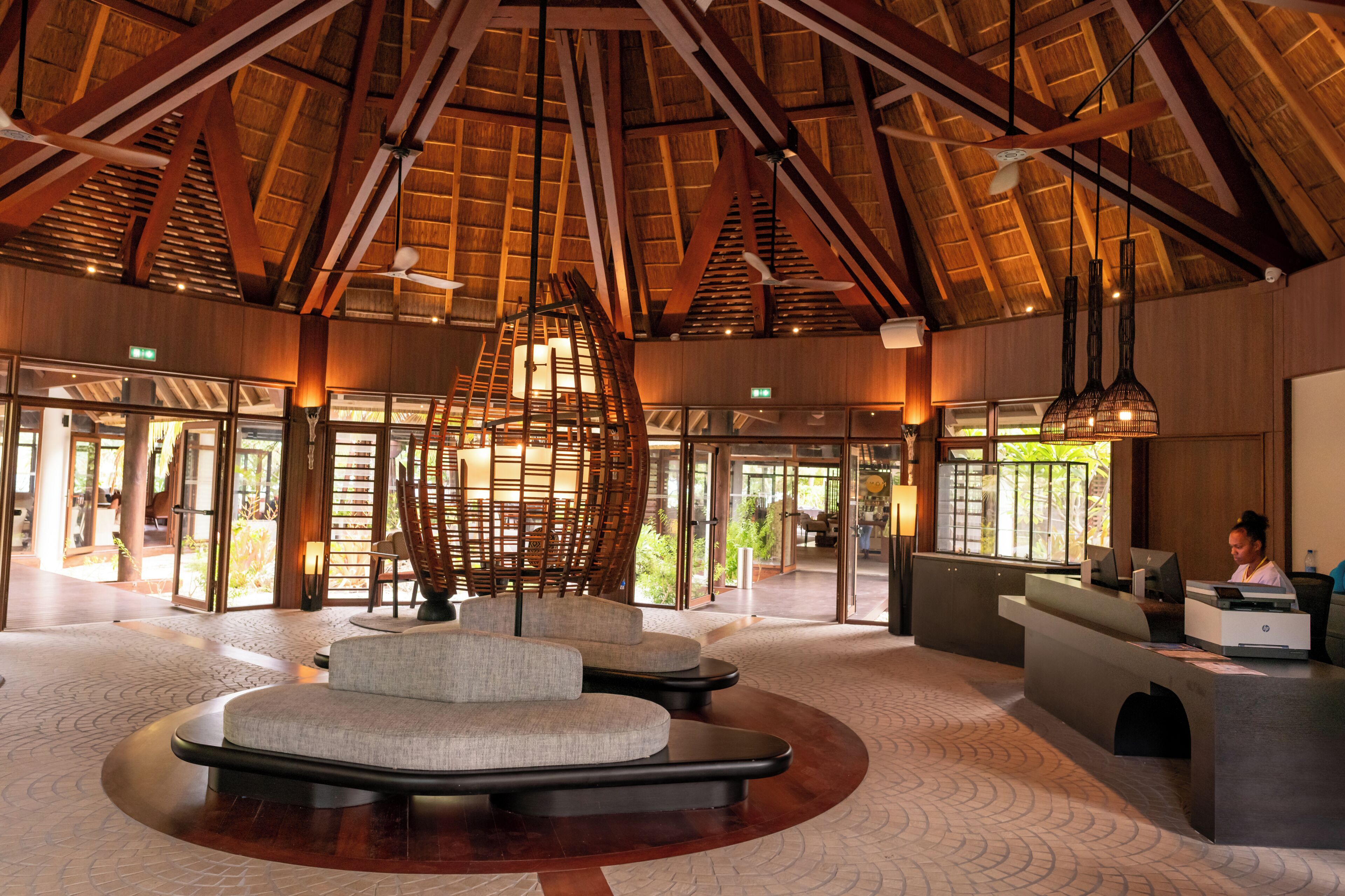 A spacious lobby with a high ceiling and natural light, featuring a reception desk, seating area, and a view of the outdoors.