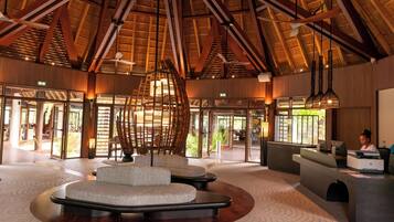 A spacious lobby with a high ceiling and natural light, featuring a reception desk, seating area, and a view of the outdoors.