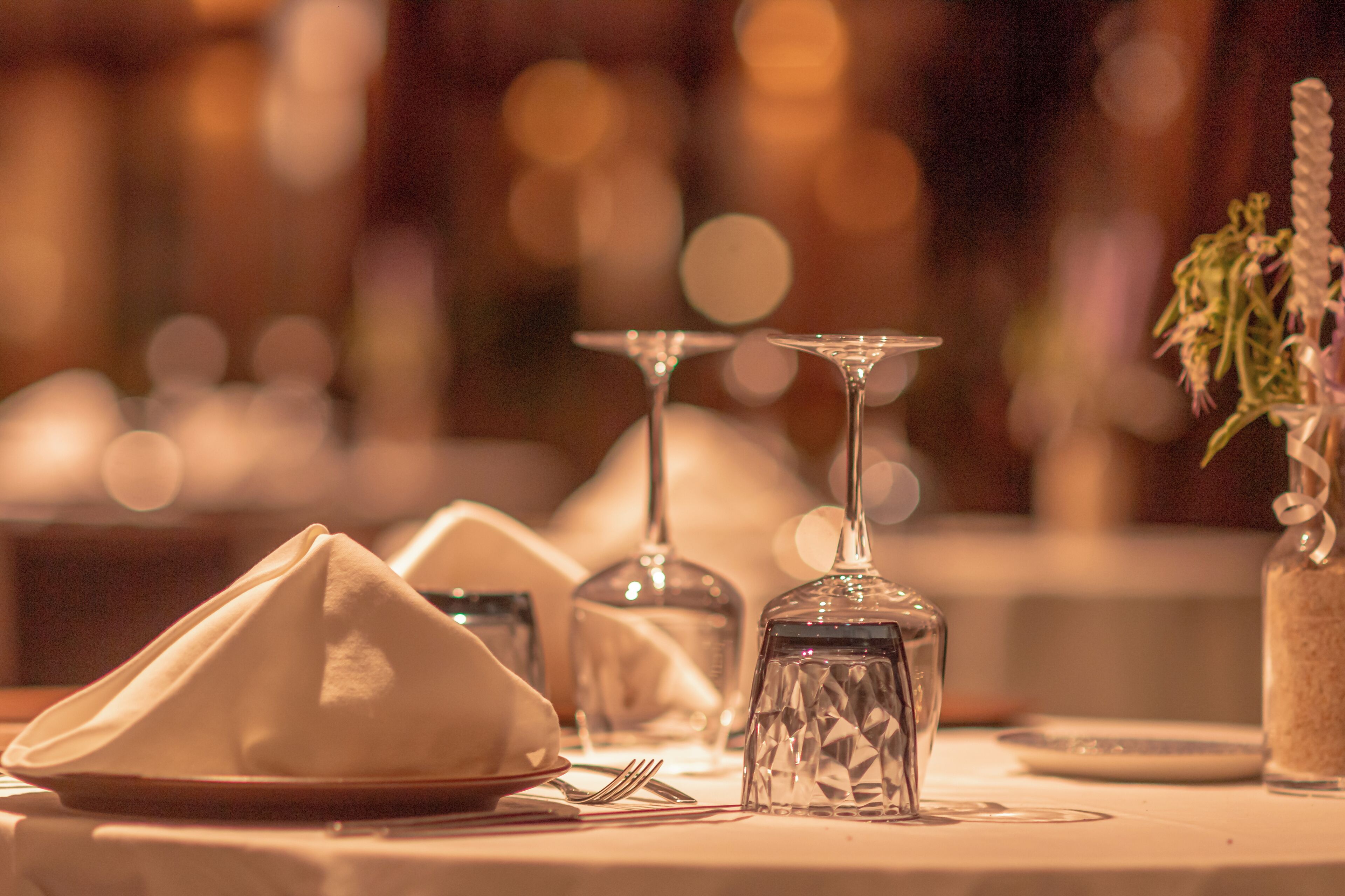 A table set with a folded napkin, a clear glass, and a glass vase with a plant.