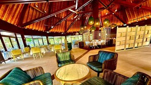 A spacious indoor area with high ceilings, round tables, and comfortable seating. - HOTEL WADRA BAY (Lifou)