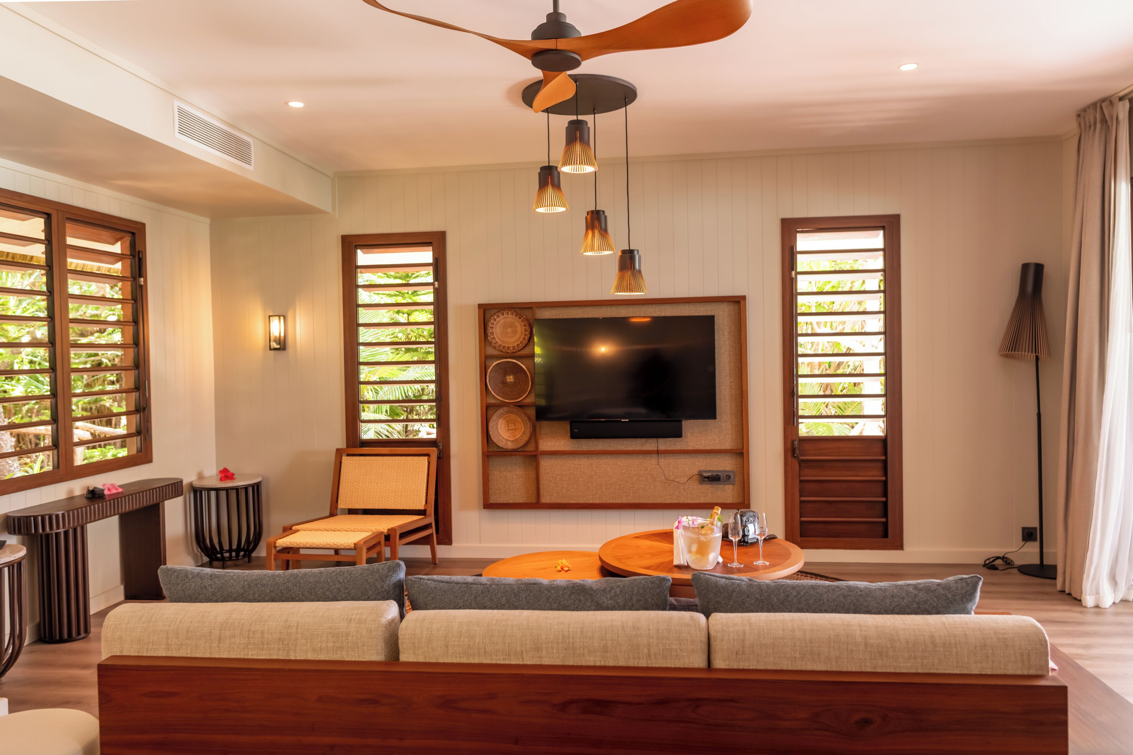 A modern living room with a sofa, a TV mounted on the wall, and a ceiling fan.