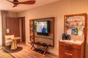 A hotel room with a television mounted on the wall, a small table with a chair, a bar area with glasses and bottles, and a wooden floor. - HOTEL WADRA BAY (Lifou)