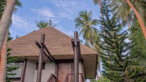 A tropical house with a thatched roof, surrounded by palm trees and a clear sky. - HOTEL WADRA BAY (Lifou)