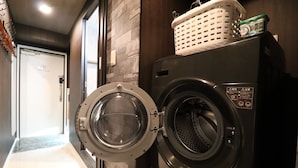 A laundry room with a front-loading washer and dryer, a basket on the dryer, and a door leading to another room. - One Stay Shinsaibashi (Osaka)