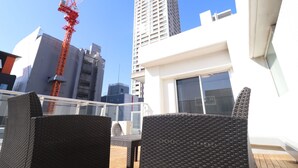 A rooftop terrace with wicker furniture, a view of a construction crane, and a tall building in the background. - One Stay Shinsaibashi (Osaka)