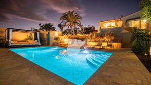 A swimming pool with a canopy and lounge chairs, surrounded by palm trees and a modern building. - CostaBlancaDreams - Casa Hella in Calpe (Calpe)