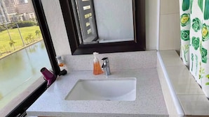 Un bagno con un lavandino bianco, mobili impiallacciati in legno, una finestra vista edifici e vegetazione, e una doccia.