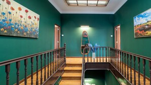 Eine Treppe mit Holzstufen und schwarzen Geländern, die zu einer Empore mit grüner Wand und einem Blumenbild führt.