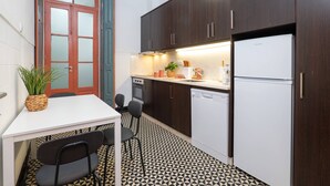 Eine kleine Küche mit dunklen Holzschränken, einem weißen Kühlschrank und einem Essbereich mit zwei Stühlen und einem Tisch.