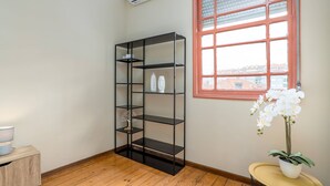 Ein Eckzimmer mit einer schwarzen Regaleinheit, einem kleinen runden Tisch mit einer Orchidee im Topf und einem Fenster mit rotem Rahmen.