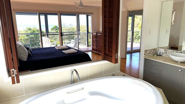 Un baño moderno con una bañera grande, un tocador con lavamanos y vistas a un balcón con cama y silla de patio.