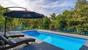 Una piscina con sillas de descanso y una sombrilla, rodeada de árboles y una valla.