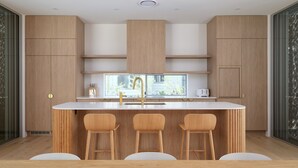 A modern kitchen with wooden cabinetry, a central island with stools, and a window providing natural light. - Navy'S By The Beach - Rainbow Shores (Rainbow Beach)