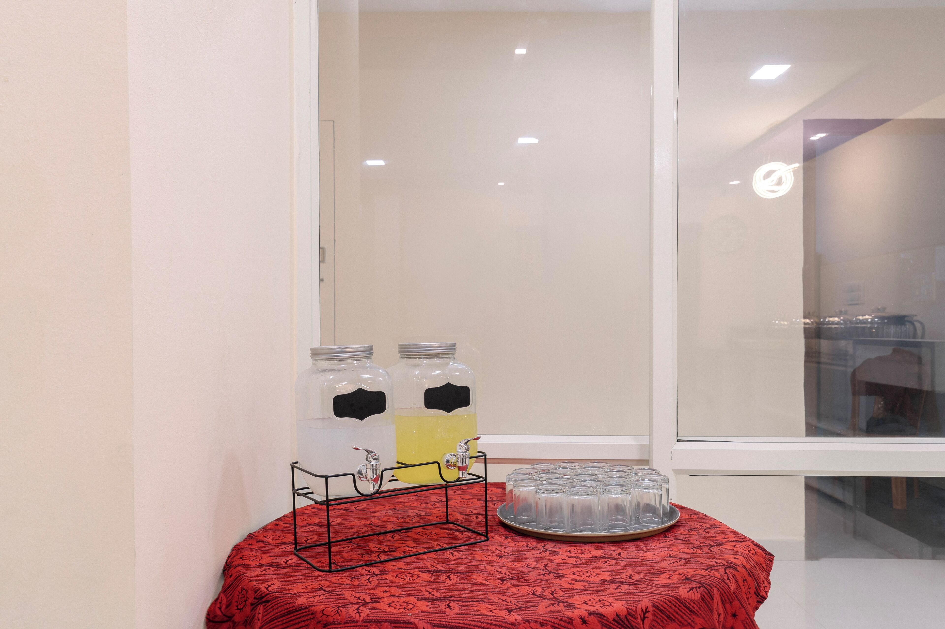 A room with a red patterned tablecloth, two beverage dispensers, and a tray of glasses.